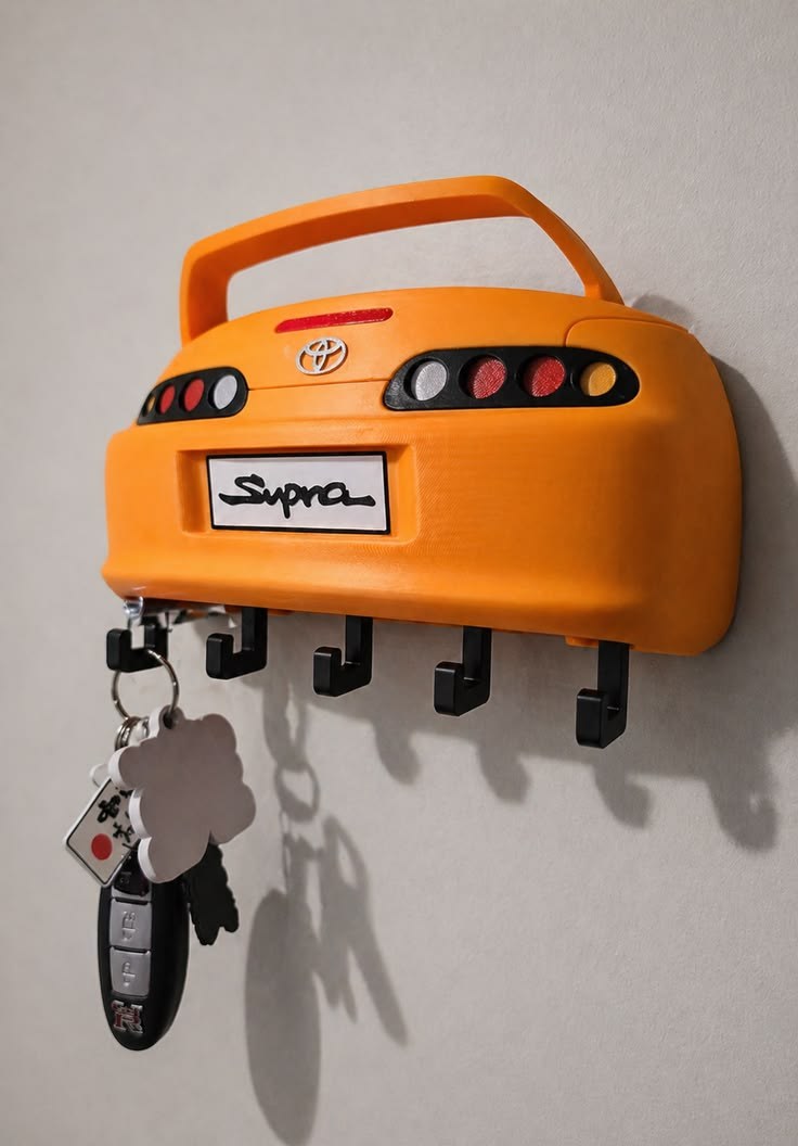 An orange 3D-printed car-shaped key holder mounted on a wall, holding keys.