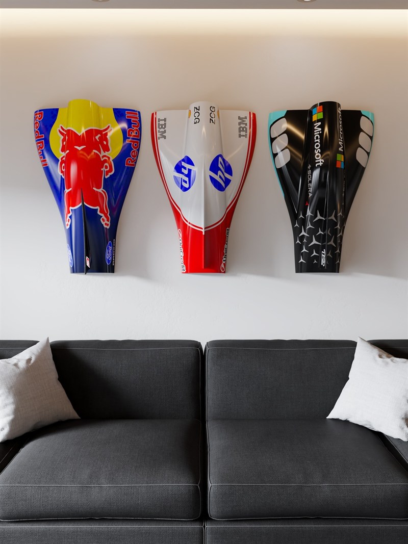 Three 3D-printed Formula 1 nose cones mounted on a wall above a dark sofa.